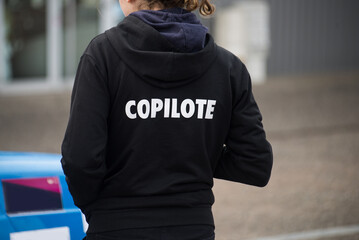 Closeup of girl wearing a black printed sweat shirt with text in french :  copilote, traduction in...