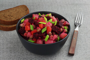 Vinaigrette traditional russian salad in a black bowl and slices of bread