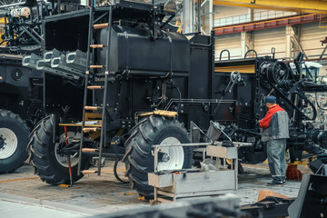 Fototapeta na wymiar Worker assembles agricultural vehicle combine harvester in industrial factory workshop.