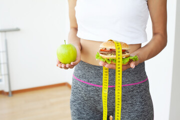 Young woman holding harmful fat burger with yellow measuring tape