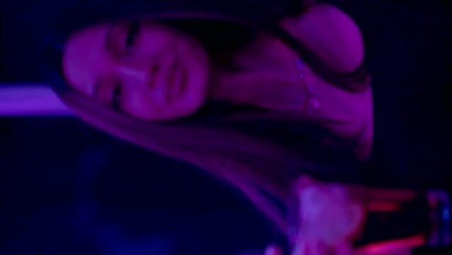 Vertical video. Close-up of a girl in a club dancing and drinking alcohol under a neon light. Night club