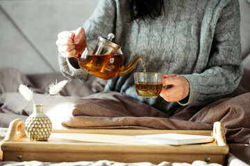 Woman pouring tea in mug from glass teapot. Cozy home hygge style interior. Breakfast still life.