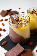 Chocolate and vanilla dessert in a jar on the stone mat and nuts in the white background..