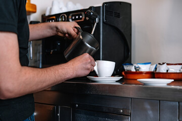 detail of a waiter's hands pouring milk into a cup of coffee. Preparing coffee with milk.