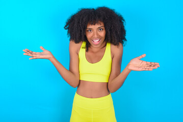 So what? Portrait of arrogant young woman with afro hairstyle in sportswear against blue background...