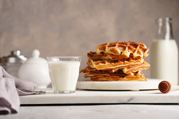 Sweet breakfast - fresh homemade belgian waffles with honey and powdered sugar stacked on white round marble board and small glass with milk
