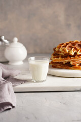 Sweet breakfast - fresh homemade belgian waffles with honey and powdered sugar stacked on white round marble board and small glass with milk