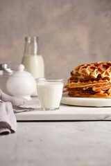 Sweet breakfast - fresh homemade belgian waffles with honey and powdered sugar stacked on white round marble board and small glass with milk