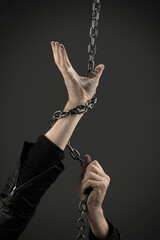 Hands entwined with iron chains on a dark background. Concept
