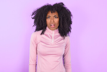 Portrait of dissatisfied young woman with afro hairstyle in technical sports shirt against purple ...