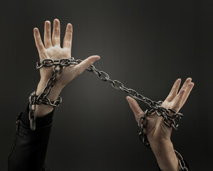 Hands entwined with iron chains on a dark background. Concept
