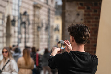 A street performer juggles a transparent acrylic ball that reflects the city on a street in Old...