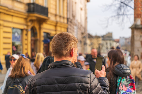 A young man holds a smartphone in his hand on the street of Old Krakow among the numerous tourists. Shooting with a smartphone