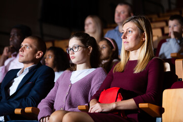 Portrait of family couple visiting theater with their teenage daughter, consumed with watching...