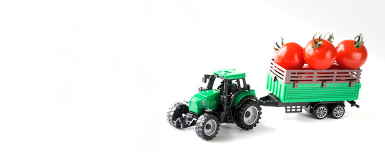 Toy tractor with a trailer loaded with fresh red cherry tomatoes. White background. The concept of...