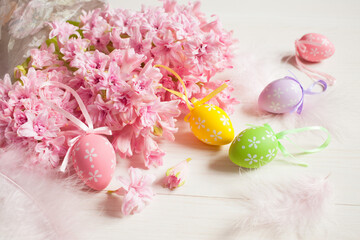 Easter greeting card, bouquet of pink hyacinth flowers and decorative colorful eggs, feathers on a white wooden table.