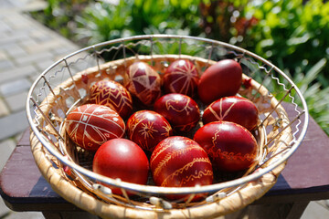 Defocus Closeup of basket of colored red eggs, Easter holiday concept. Modern painted easter eggs. Nature background, garden. Collection of pysanka or krashanka. Out of focus