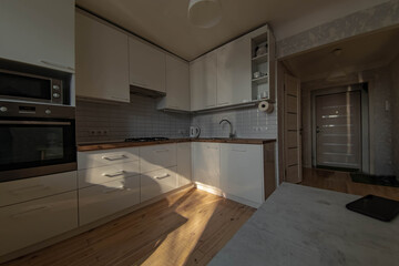 interior of a small sunny kitchen with wooden floor and white cabinets, solid wood worktop.