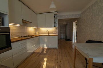 interior of a small cozy kitchen with wooden floor and white furniture, sunbeams in the room.