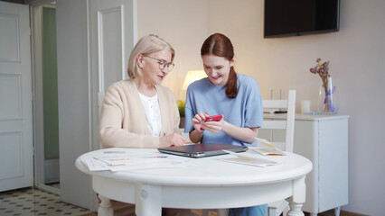 A pensioner with glasses and her adult daughter look at photos on the phone, comment and discuss