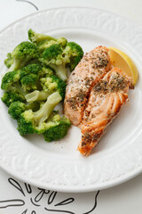 Grilled salmon served with broccoli and a piece of lemon on white plate. Vegetarian lunch for diet.