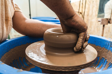 Hands of a potter working clay on a potter's wheel. The clay takes the shape the potter gives it with the terracotta tone of the clay.