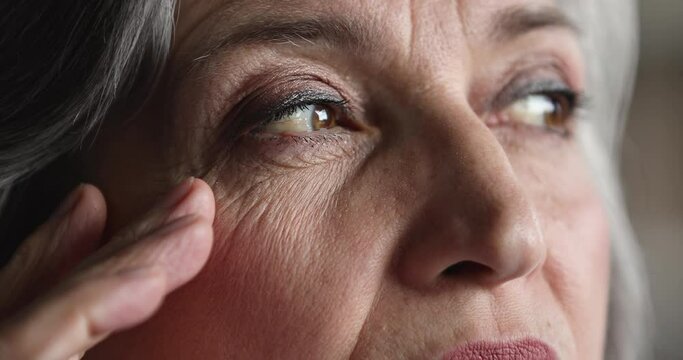 Extreme cropped view of older pensive serious female wrinkled face, staring aside looks tired, thinks, feels troubled. Close up of aged woman eyes, eyesight vision check up clinic services ad concept