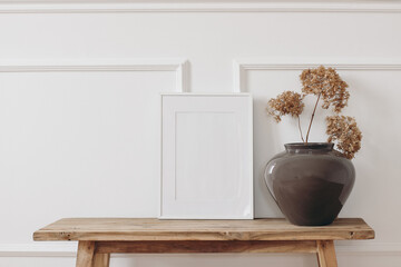 Brown bold vase. Dry hydrangea flowers on old wooden bench. Blank black picture frame mockup. White...