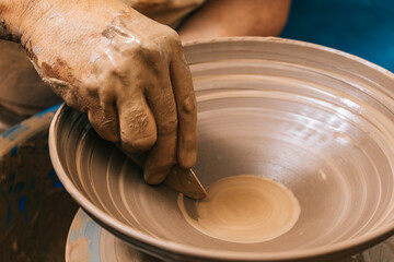 Hands of a potter working clay on a potter's wheel. The clay takes the shape the potter gives it with the terracotta tone of the clay.