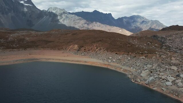 Aerial orbit of Laguna negra deep lagoon between Andean mountains, Meson Anto Hill and Glacier in background, Cajon del Maipo, Chile