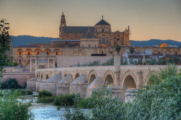 Sunset view of the old roman bridge in the spanish city cordoba with the la mezquita cathedral on horizon.