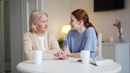 A woman volunteer and an elderly lady are sitting in the living room and chatting while having tea