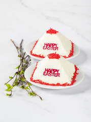 Festive dessert. Cottage cheese creamy Easter, decorated with red confectionery sprinkles, on a plate with spring birch twigs. Light background