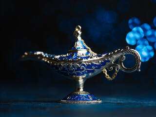 Aladdin's magical lamp, jeweled on a blue background. Arabian fairy tales, wish fulfillment symbol,...