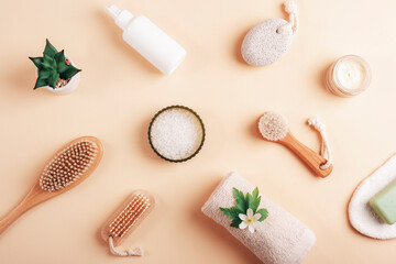 Fototapeta na wymiar Cosmetic flat lay on neutral beige background. Towel, sea salt, face and body brushes, pumice stone, soap, face cream and body lotion. Spa and wellness concept. Top view
