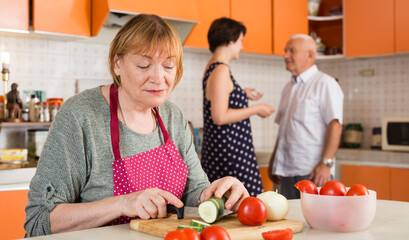 Portrait of smiling mature housewife preparing family dinner at kitchen table..