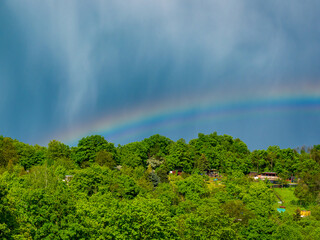 Rainbow over the hill with several garden houses a few moments after heavy rain