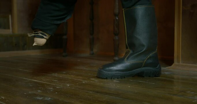 Pirate captain breaks sawed light brown wooden leg prosthesis standing in black boot ON floor in cabin of pirates ship at voyage closeup