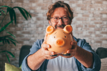 Happy mature man showing piggy bank to save money. Caucasian male holding money box for investment and future planning concept. Portrait of confident guy holding coin bank and smiling