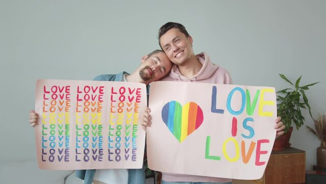 Two young handsome guys are showing lgbt posters, looking at each other and smiling