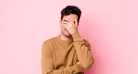 handsome hispanic man looking stressed, ashamed or upset, with a headache, covering face with hand