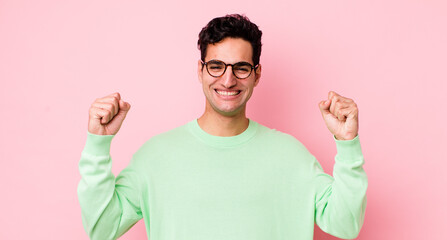 handsome hispanic man feeling happy, positive and successful, celebrating victory, achievements or...