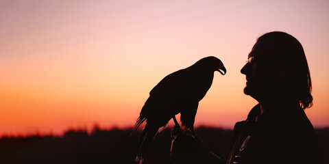 Banner Silhouette of man and wild bird over sunset sky looking on each other Buzzard or eagle symbol of power, victory, courage, greatness and spiritual uplift, brave person in eye glasses, vision