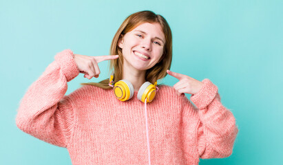 red head pretty woman smiling confidently pointing to own broad smile. headphones and music concept