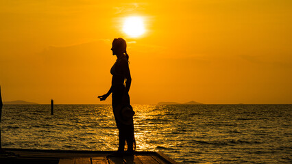 Silhouette young woman on wood bridge with sunset. cheering happy woman open arms to sunrise at seaside.