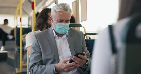 Older man in suit rides public transportation bus, businessman has protective mask on face receives phone call on smartphone, talks to friend - Powered by Adobe