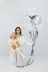 Woman with blonde daughter in white studio with balloons. Festive decoration. Children's happiness. Valentine's Day.