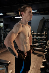 Fototapeta na wymiar Seriuous fit young man with perfect abs muscles resting between exercise sets in gym