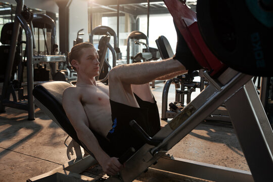 Concentrated athletic young man in sportswear doing exercise on legs press machine in gym