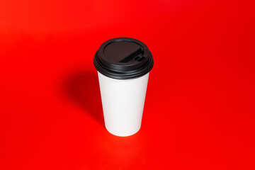 Paper disposable cup for coffee to go on a red background, place for text